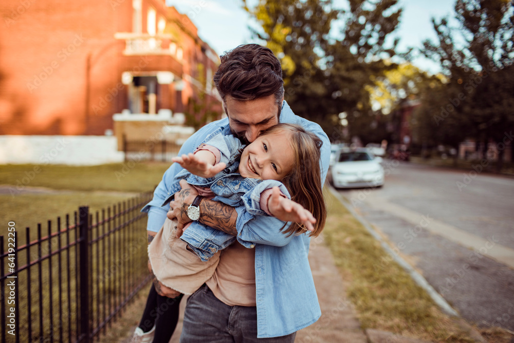 A father embracing his daughter on a tree-lined residential street